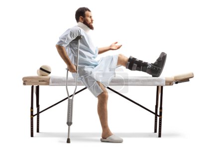 Téléchargez les photos : Patient blessé à la jambe assis sur un lit pour une thérapie physique isolé sur fond blanc - en image libre de droit