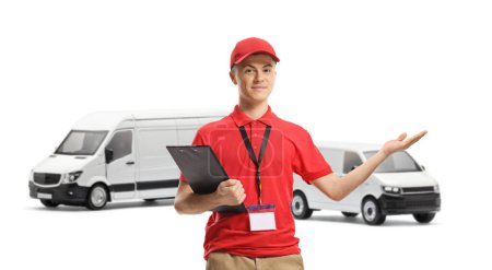 Photo for Young courier holding a clipboard and gesturing with hand in front of transport vans isolated on white background - Royalty Free Image