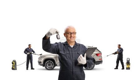 Téléchargez les photos : Hommes travaillant à un lavage de voiture et montrant une clé de voiture isolée sur fond blanc - en image libre de droit