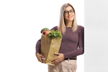 Photo for Young woman holding a grocery bag and leaning on a wall isolated on white background - Royalty Free Image