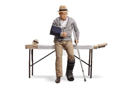 Photo for Senior man with a broken arm and leg sitting on a bed for physical therapy isolated on white background - Royalty Free Image