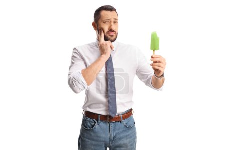 Téléchargez les photos : Jeune homme avec une crème glacée sucette tenant sa joue et ayant un mal de dents isolé sur fond blanc - en image libre de droit