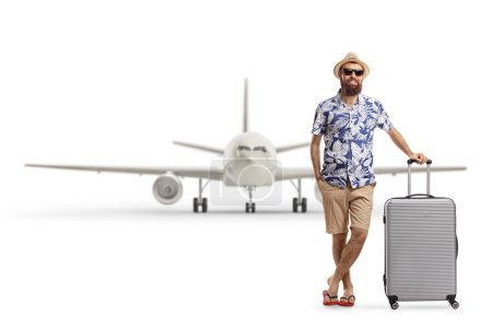 Photo for Full length portrait of a bearded male tourist posing with a suitcase in front of a plane isolated on white background - Royalty Free Image