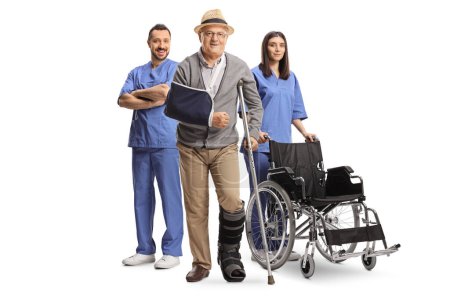 Téléchargez les photos : Équipe de travailleurs médicaux derrière un patient âgé avec un bras cassé isolé sur fond blanc - en image libre de droit