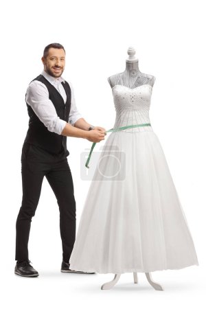 Téléchargez les photos : Tailleur mesurant une robe de mariée sur un mannequin poupée isolé sur fond blanc - en image libre de droit