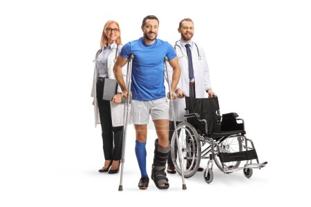 Foto de Retrato de cuerpo entero de un atleta masculino con muletas y un aparato ortopédico delante de médicos aislados sobre fondo blanco - Imagen libre de derechos