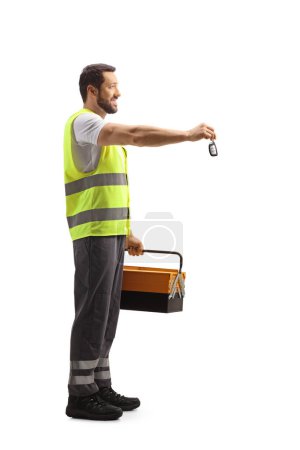 Téléchargez les photos : Plan de profil complet d'un travailleur de la route dans un gilet réfléchissant tenant une boîte à outils et reprenant une clé de voiture isolée sur fond blanc - en image libre de droit
