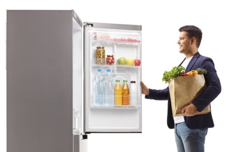 Photo for Man with a grocery bag opening a fridge door isolated on white background - Royalty Free Image