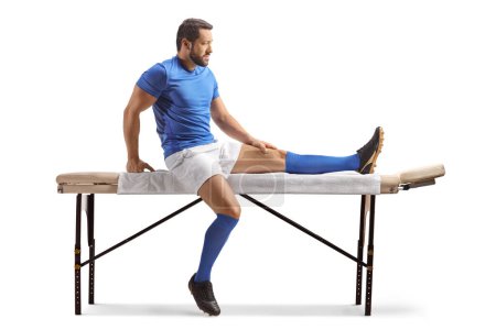 Téléchargez les photos : Joueur de football assis sur un lit de massage isolé sur fond blanc - en image libre de droit