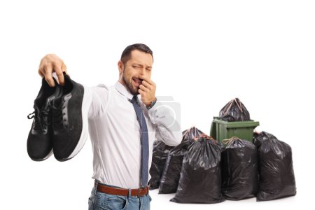 Photo for Man holding a pair of smelly trainers in front of waste bins isolated on white background - Royalty Free Image