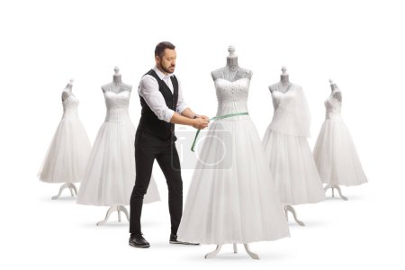 Téléchargez les photos : Tailleur prenant des mesures à partir d'une robe de mariée sur un mannequin poupée isolé sur fond blanc - en image libre de droit