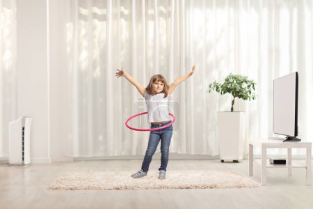 Photo for Full length portrait of a little girl spinning a hula hoop at home in a living room - Royalty Free Image