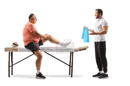 Photo for Physical therapist showing exercise to a mature man with an injured knee isolated on white background - Royalty Free Image