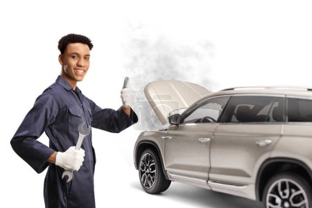 Photo for African american car mechanic holding a wrench and gesturing thumbs up in front of a broken down SUV isolated on white backgroun - Royalty Free Image