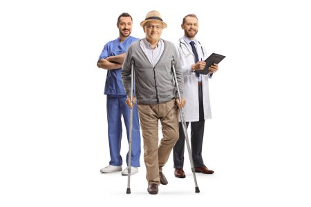 Foto de Retrato completo de un hombre mayor con muletas y trabajadores médicos en la espalda aislados sobre fondo blanco - Imagen libre de derechos
