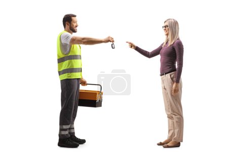 Photo for Full length profile shot of a road assistance agent in a reflective vest giving a car key to a casual woman isolated on white background - Royalty Free Image