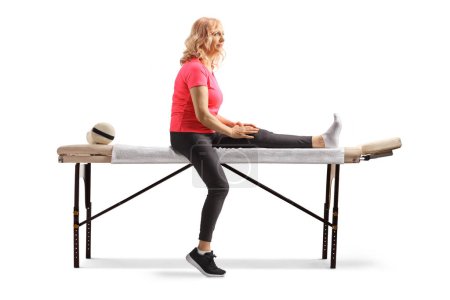 Téléchargez les photos : Femme mûre avec un pied blessé assis sur une table de thérapie isolé sur fond blanc - en image libre de droit