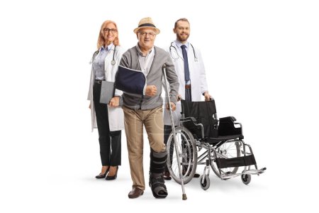 Téléchargez les photos : Portrait complet d'un patient âgé avec des béquilles et des médecins dans le dos isolé sur fond blanc - en image libre de droit