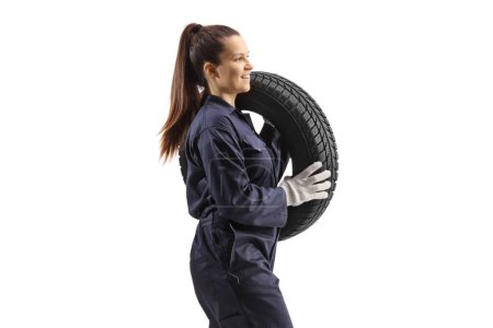Photo for Profile shot of a female auto mechanic carrying a vehicle tire and walking isolated on white background - Royalty Free Image