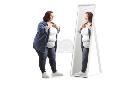 Téléchargez les photos : Surpoids occasionnel jeune femme se préparer devant un miroir isolé sur fond blanc - en image libre de droit
