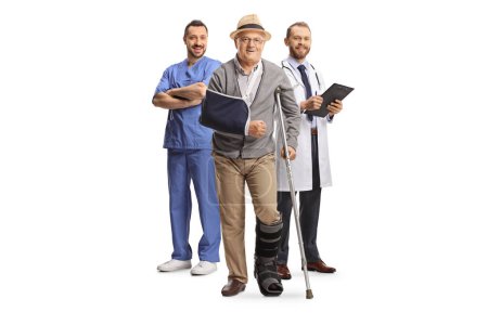 Téléchargez les photos : Portrait complet d'un homme âgé avec une béquille et des médecins debout dans le dos isolé sur fond blanc - en image libre de droit