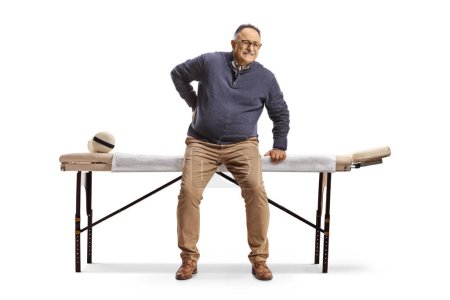 Téléchargez les photos : Homme mûr avec un dos raide assis à une table de massage isolé sur fond blanc - en image libre de droit