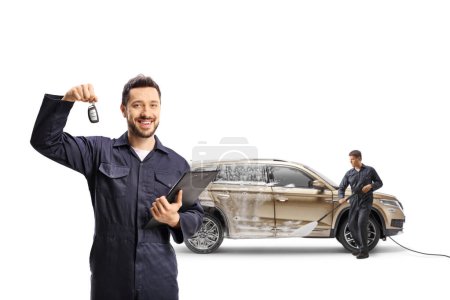Téléchargez les photos : Travailleurs nettoyant un 4x4 à un lavage de voiture et tenant une clé de voiture isolée sur fond blanc - en image libre de droit