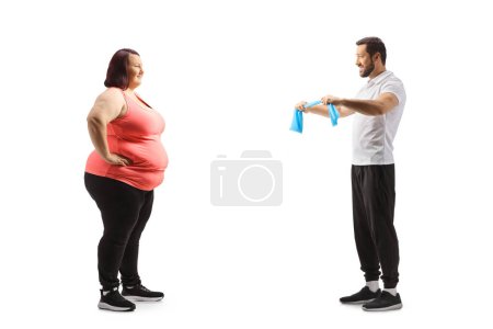 Téléchargez les photos : Photo de profil pleine longueur d'un entraîneur de fitness montrant un exercice à une jeune femme en surpoids isolée sur fond blanc - en image libre de droit