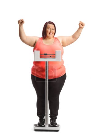 Foto de Mujer con sobrepeso en ropa deportiva de pie en una escala médica y el gesto de felicidad aislado en el fondo blanco - Imagen libre de derechos