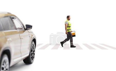 Foto de Mecánico de asistencia vial caminando en un paso peatonal frente a un SUV y llevando una caja de herramientas aislada sobre fondo blanco - Imagen libre de derechos