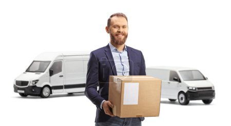 Photo for Young man standing and holding a cardboard box in front of transport vans isolated on white background - Royalty Free Image