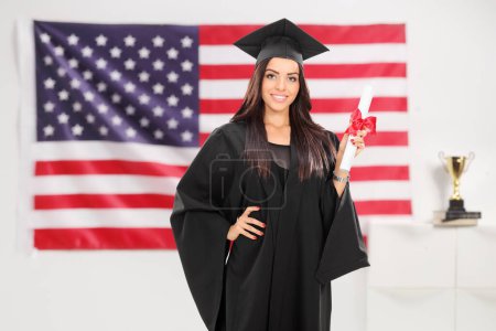 Photo for Female graduate student holding a diploma in front of an american flag - Royalty Free Image
