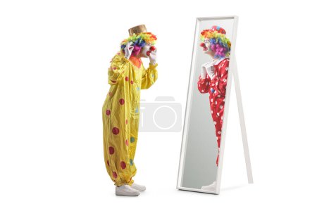 Téléchargez les photos : Clown en costume jaune debout devant un miroir et regardant un clown en costume rouge isolé sur fond blanc - en image libre de droit