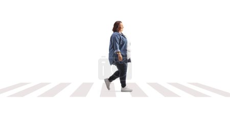 Photo for Full length profile shot of an overweight woman in casual clothing walking at a pedestrian crossing isolated on white background - Royalty Free Image