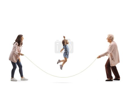 Foto de Pequeño gitl saltando una cuerda y jugando con madre y abuela aisladas sobre fondo blanco - Imagen libre de derechos
