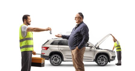 Foto de Mecánico comprobando un SUV y dando llaves de coche a un hombre maduro aislado sobre fondo blanco - Imagen libre de derechos