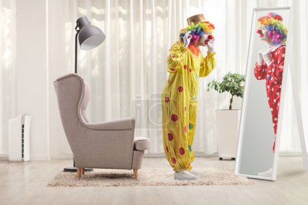 Photo for Clown in a yellow costume standing in front of a mirror and looking at a clown in a red costume in a room - Royalty Free Image