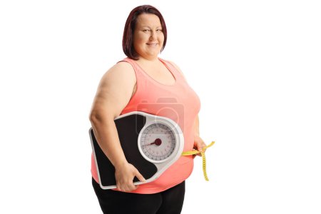 Foto de Mujer con sobrepeso sonriente sosteniendo una balanza y midiendo la cintura aislada sobre fondo blanco - Imagen libre de derechos