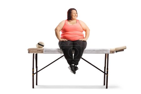 Foto de Mujer con sobrepeso sentada en una cama para fisioterapia aislada sobre fondo blanco - Imagen libre de derechos