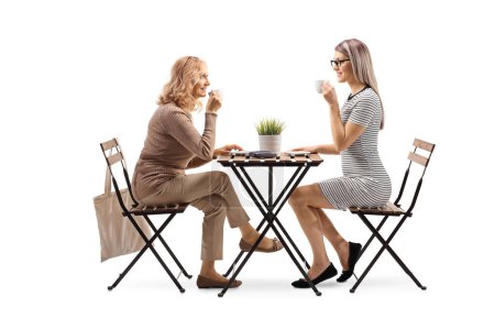 Téléchargez les photos : Deux femmes assises à une table et buvant du café isolé sur fond blanc - en image libre de droit