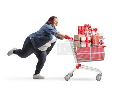 Photo for Full length profile shot of a corpulent woman running with a shopping cart full of presents isolated on white background - Royalty Free Image