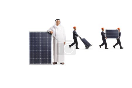 Foto de Hombre árabe de pie junto a un panel solar y trabajadores llevando paneles en la espalda aislados sobre fondo blanco - Imagen libre de derechos