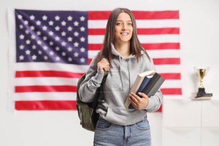 Photo for Smiling female student holding books and posing in front of an american flag - Royalty Free Image