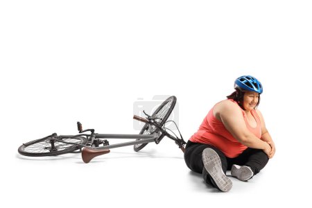 Photo for Female bicycle rider sitting on the ground and holding an injured knee isolated on white background - Royalty Free Image