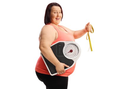 Photo for Cheerful overweight woman holding a tape and a weight scale isolated on white background - Royalty Free Image