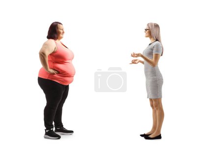 Photo for Full length profile shot of a slim woman talking to an overweight young woman in sportswear isolated on white background - Royalty Free Image