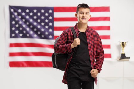 Téléchargez les photos : Adolescent avec un sac à dos souriant à la caméra devant un drapeau des États-Unis - en image libre de droit
