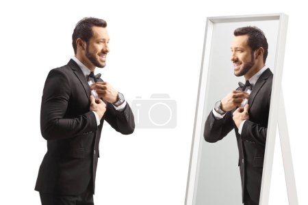 Téléchargez les photos : Jeune homme élégant se préparant devant un miroir isolé sur fond blanc - en image libre de droit