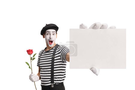 Téléchargez les photos : Mime tenant une rose rouge et montrant une carte vierge isolée sur fond blanc - en image libre de droit