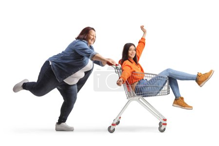 Foto de Foto de perfil completo de una mujer con sobrepeso empujando a un amigo dentro de un carrito de compras aislado sobre fondo blanco - Imagen libre de derechos